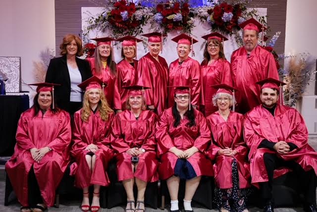 Bible Institute graduates in red caps and gowns, gathered with Pastor Kimberley for their class photo