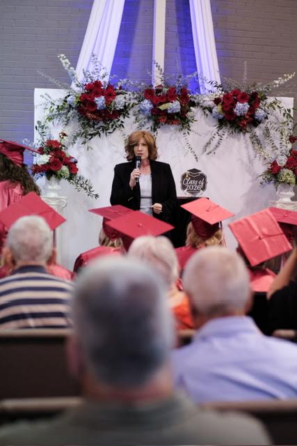 Pastor Kimberley speaking to the graduating class at Bible Institute commencement, red caps in the foreground